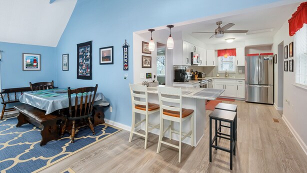 Una cocina moderna con armarios blancos, electrodomésticos de acero inoxidable y un comedor con pared azul y sillas de madera.