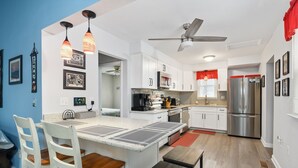 Una cocina moderna con armarios blancos, electrodomésticos de acero inoxidable y un comedor con mesa y sillas.