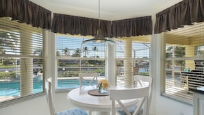 Habitación de esquina con vista a la piscina, muebles blancos y cortinas oscuras.
