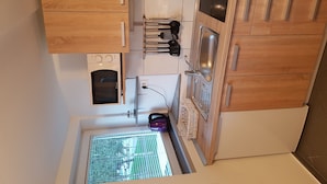 Eine kleine Küche mit Holdekor-Schränken, einem Backofen, einer Spüle und einem Fenster mit Blick auf Grünflächen.