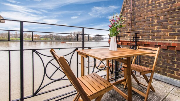 A wooden table and chairs on a balcony with a brick wall and a metal railing. - River View, Penthouse Apartment, Zone 2, Hammersmith, London, 2 Bedrooms  2 Bath (London)