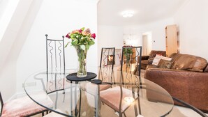 A modern living room with a glass dining table, a brown leather sofa, and a fireplace in the background. - River View, Penthouse Apartment, Zone 2, Hammersmith, London, 2 Bedrooms  2 Bath (London)