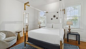 Un letto a baldacchino con lenzuola bianche, una poltrona rotonda e un comodino con una lampada.