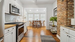Una cucina moderna con mobili bianchi, un microonde in acciaio inossidabile e una parete decorata con mattoni.