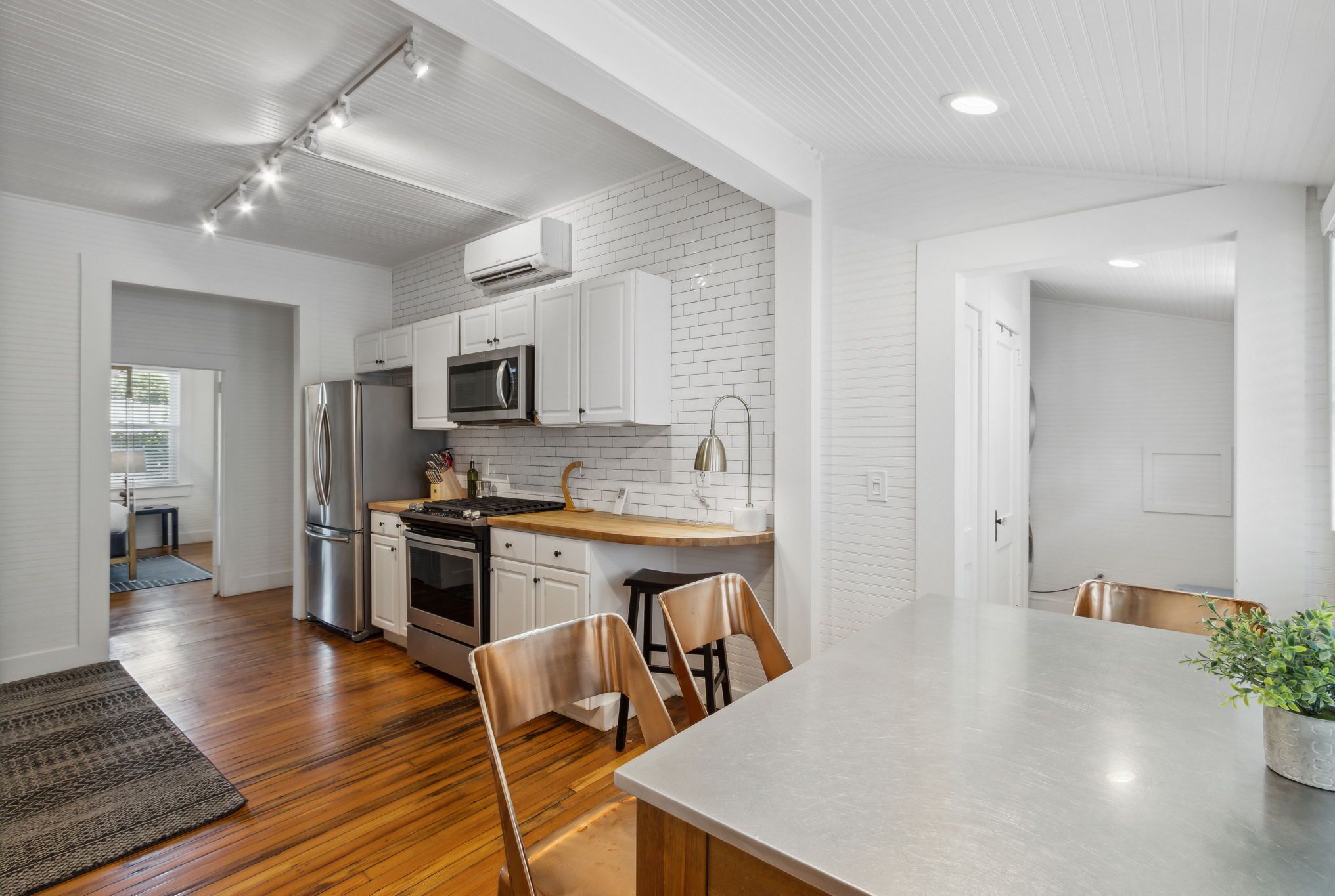 Una cocina moderna con armarios blancos, electrodomésticos de acero inoxidable y suelo de madera.
