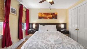 A hotel room with a bed, two bedside tables, a ceiling fan, a wall-mounted artwork, and a door. - Steps to Commercial St Walk to Beach! (Provincetown)
