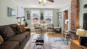 A living room with a sofa, chairs, a coffee table, a fireplace, and a ceiling fan. - Steps to Commercial St Walk to Beach! (Provincetown)