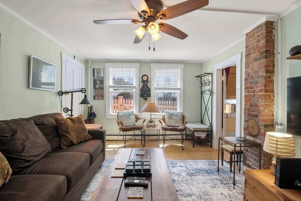 A living room with a sofa, chairs, a coffee table, a fireplace, and a ceiling fan.