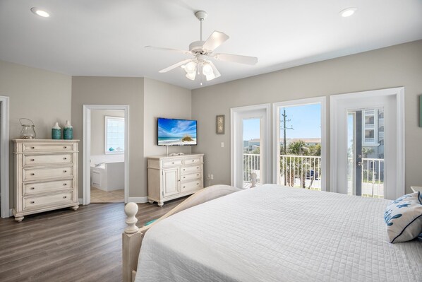 A bedroom with a bed, dresser, TV, and balcony doors.