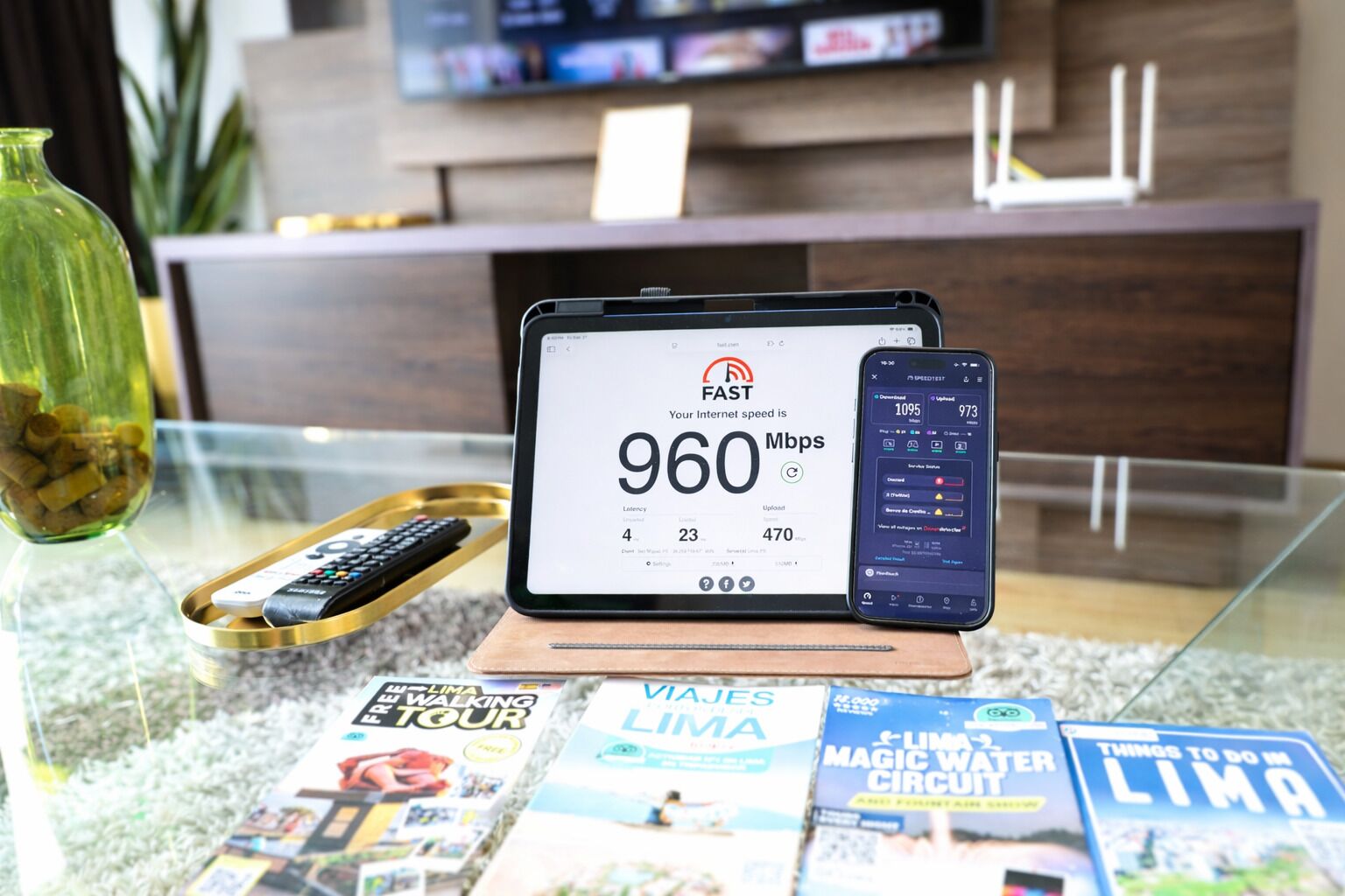 Una tableta mostrando resultados de una prueba de velocidad de internet, un teléfono inteligente y folletos de viajes sobre una mesa de vidrio.