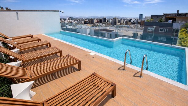 A rooftop pool with wooden loungers and a city view. - Miraflores Nest - Upper Pardo (Miraflores)