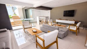A modern living room with a sofa, chairs, a coffee table, a TV, and a kitchen area. - Miraflores Nest - Upper Pardo (Miraflores)