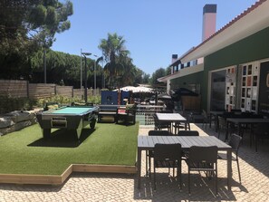 Zona de piscina al aire libre con una mesa y sillas, rodeada por una valla de madera y árboles.