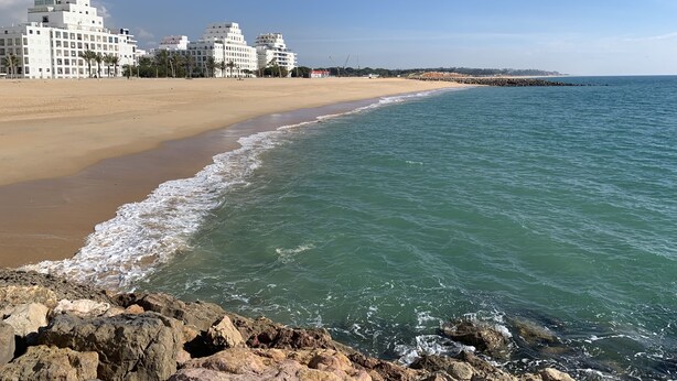 A beach with a rocky shoreline, a sandy beach, and a row of white buildings in the background.
