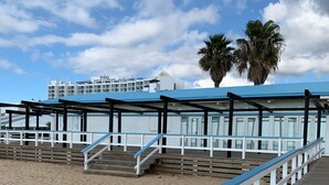 A beachside boardwalk with a blue railing, leading to a building with a blue roof and white walls.
