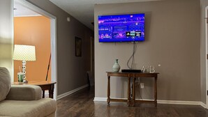 Een woonkamer met een plafondventilator, een flatscreen televisie aan de muur, een houten salontafel en een beige bank.