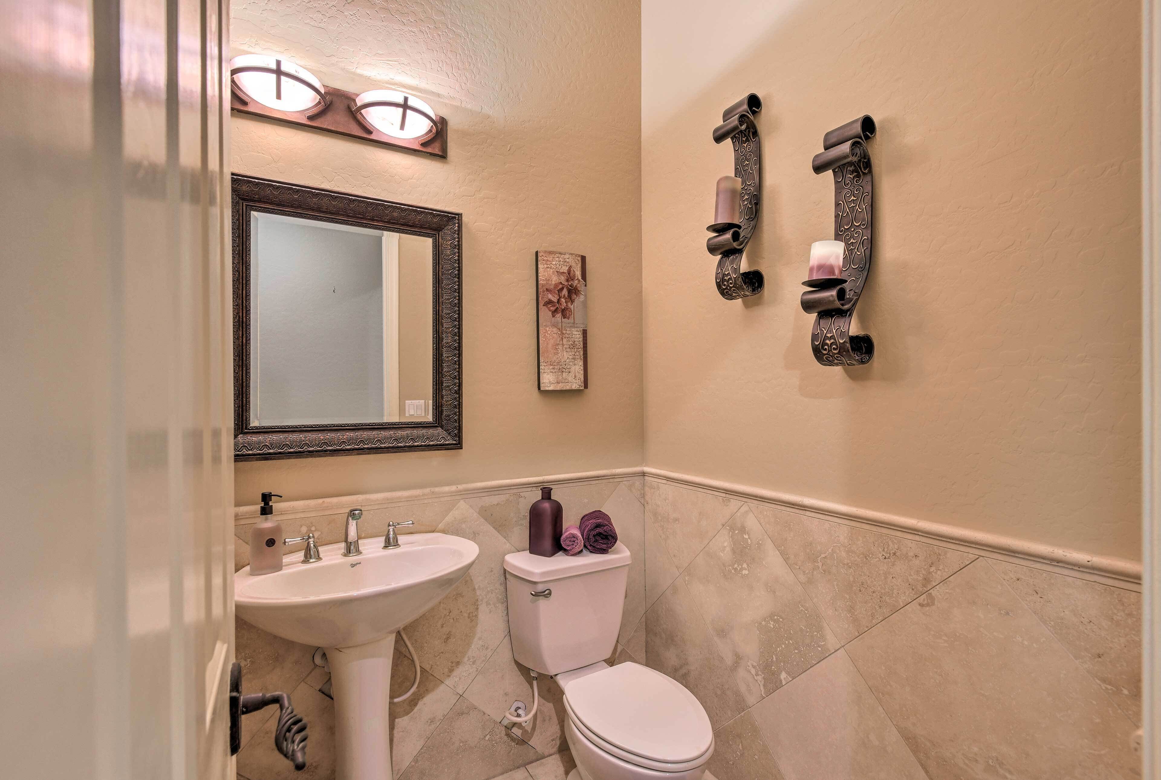 Un bagno con lavandino, WC e specchio bianchi. Due portasci da parete e un elemento decorativo sopra lo specchio.