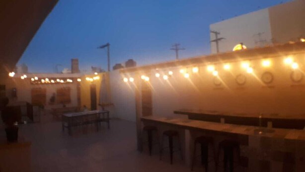 Un patio al aire libre con mesas y sillas, una zona de bar con taburetes y vistas del horizonte de la ciudad al atardecer.