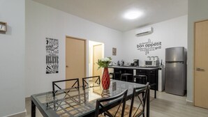 Una cocina moderna con un refrigerador de acero inoxidable, un comedor con una mesa de vidrio y sillas tejidas, y decoración motivacional en la pared.