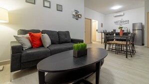 Un apartamento moderno con un sofá gris, una mesa de centro redonda y una zona de comedor con una cocina al fondo.