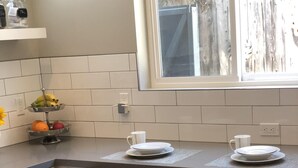 A modern kitchen with white subway tiles, a window with a view of a wooden fence, and a bar area with three stools. - Perfectly located, Modern, custom built casita w/AC & rooftop igloo sunset deck (San Diego)