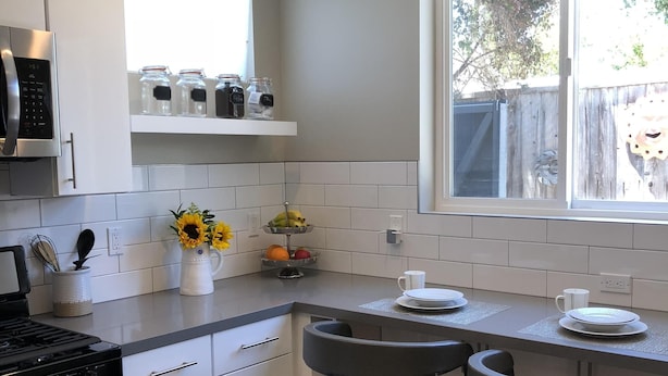 A modern kitchen with white cabinets, a stainless steel stove, and a window with a view of the backyard. - Perfectly located, Modern, custom built casita w/AC & rooftop igloo sunset deck (San Diego)