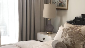A neatly made bed with a white duvet, a decorative lamp on a bedside table, and a framed artwork on the wall. - Perfectly located, Modern, custom built casita w/AC & rooftop igloo sunset deck (San Diego)