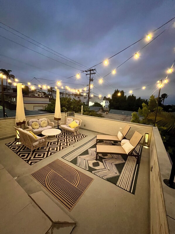An outdoor seating area with patterned rugs, lounge chairs, and string lights. - Perfectly located, Modern, custom built casita w/AC & rooftop igloo sunset deck (San Diego)