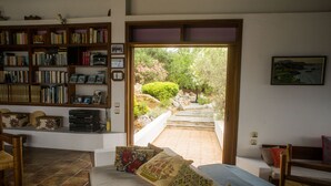 A room with a bed, a bookshelf, and a view of a garden through an open door. - Architect designed Cretan Sea Vista (Chania)