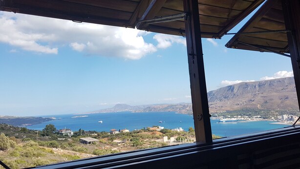 A view from a covered balcony overlooking a coastal area with buildings and mountains in the distance. - Architect designed Cretan Sea Vista (Chania)