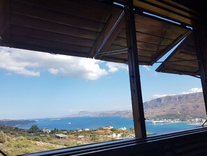 A view from a covered balcony overlooking a coastal area with buildings and mountains in the distance. - Architect designed Cretan Sea Vista (Chania)