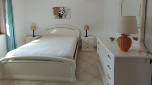 A bedroom with a bed, two bedside tables with lamps, a dresser, a mirror, and an air conditioning unit. - House in Teulada for 4 people a few minutes from the beautiful beaches  (Teulada)