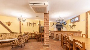 A dining area with a brick column, wooden furniture, a fireplace, and wall-mounted lights. - Alval House for 23 people (Villacastín)