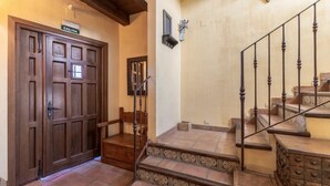 A wooden door with a sign reading "SALIDA" (exit), a wooden bench, a staircase with ornate railings, and a wall-mounted light fixture. - Alval House for 23 people (Villacastín)