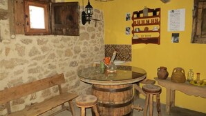 A rustic room with a stone wall, wooden bench, round wooden table, stools, and a shelf with pottery. - Your Village House Tiétar Valley (La Iglesuela)
