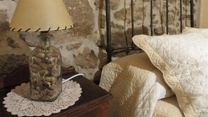 A bed with a white quilt, a lamp on a wooden nightstand, and a stone wall. - Your Village House Tiétar Valley (La Iglesuela)