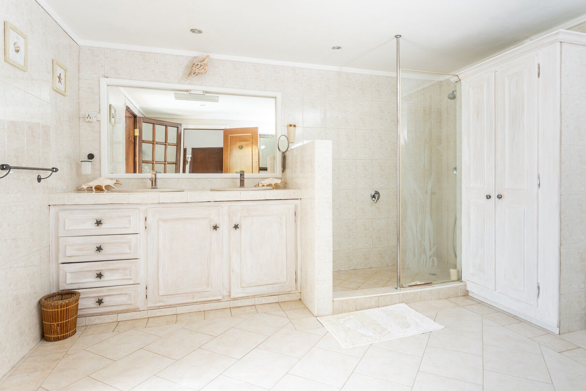 A bathroom with a large mirror, a shower enclosure, and a vanity with drawers.
