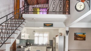 Una cocina amplia con una isla central, un comedor con sillas, una escalera y un reloj en la pared.