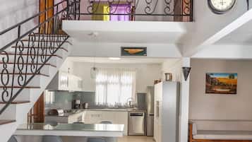 A spacious kitchen with a central island, a dining area with chairs, a staircase, and a clock on the wall.