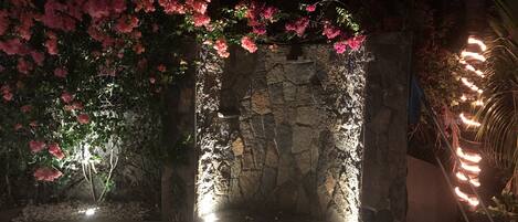 Een stenen muur met roze bloemen en lichtjes, een zwembad en een pad van stenen.