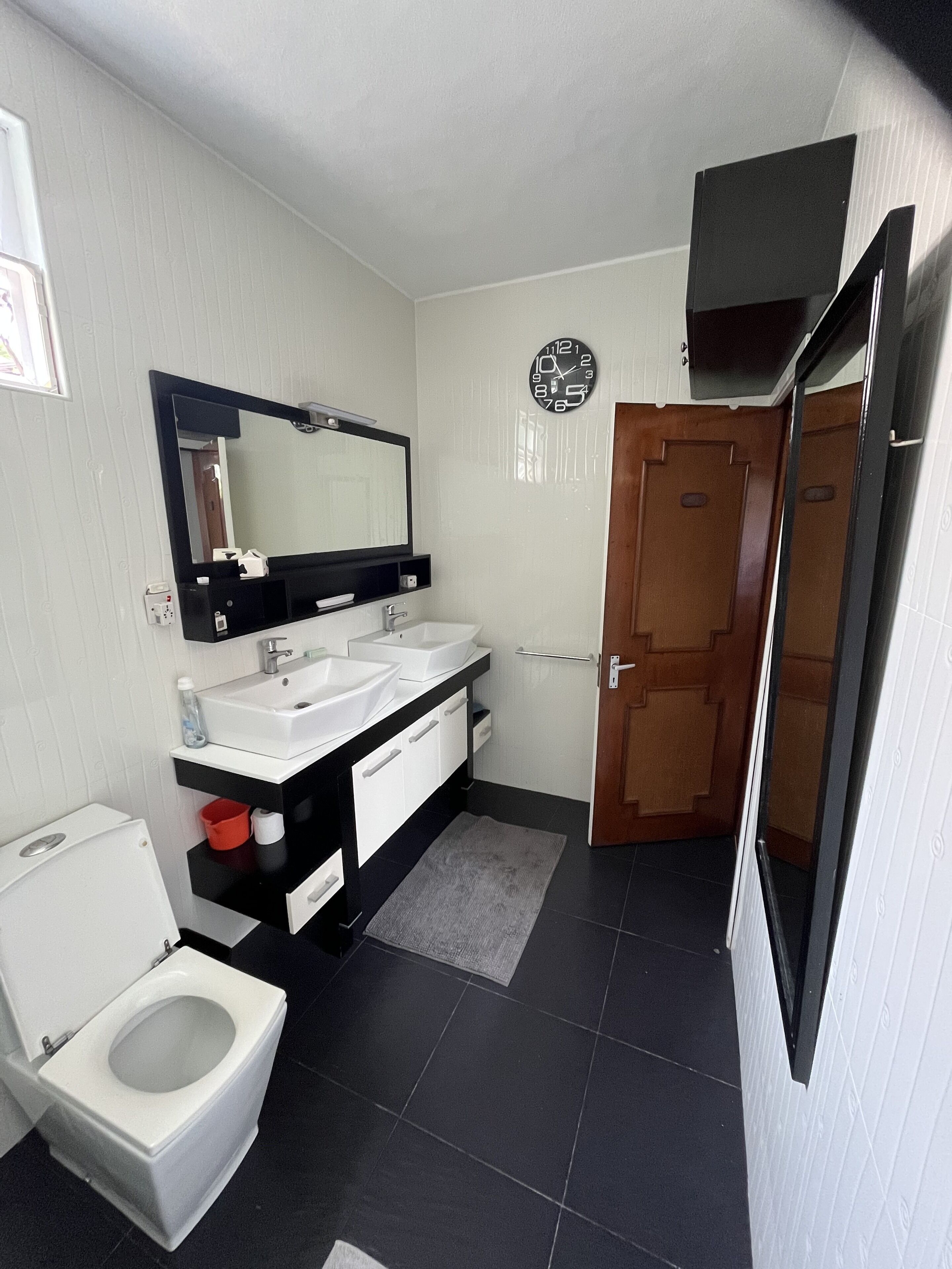 Ein Badezimmer mit Toilette, Waschbecken mit Spiegel darüber, einer Holztür und einer Uhr an der Wand.