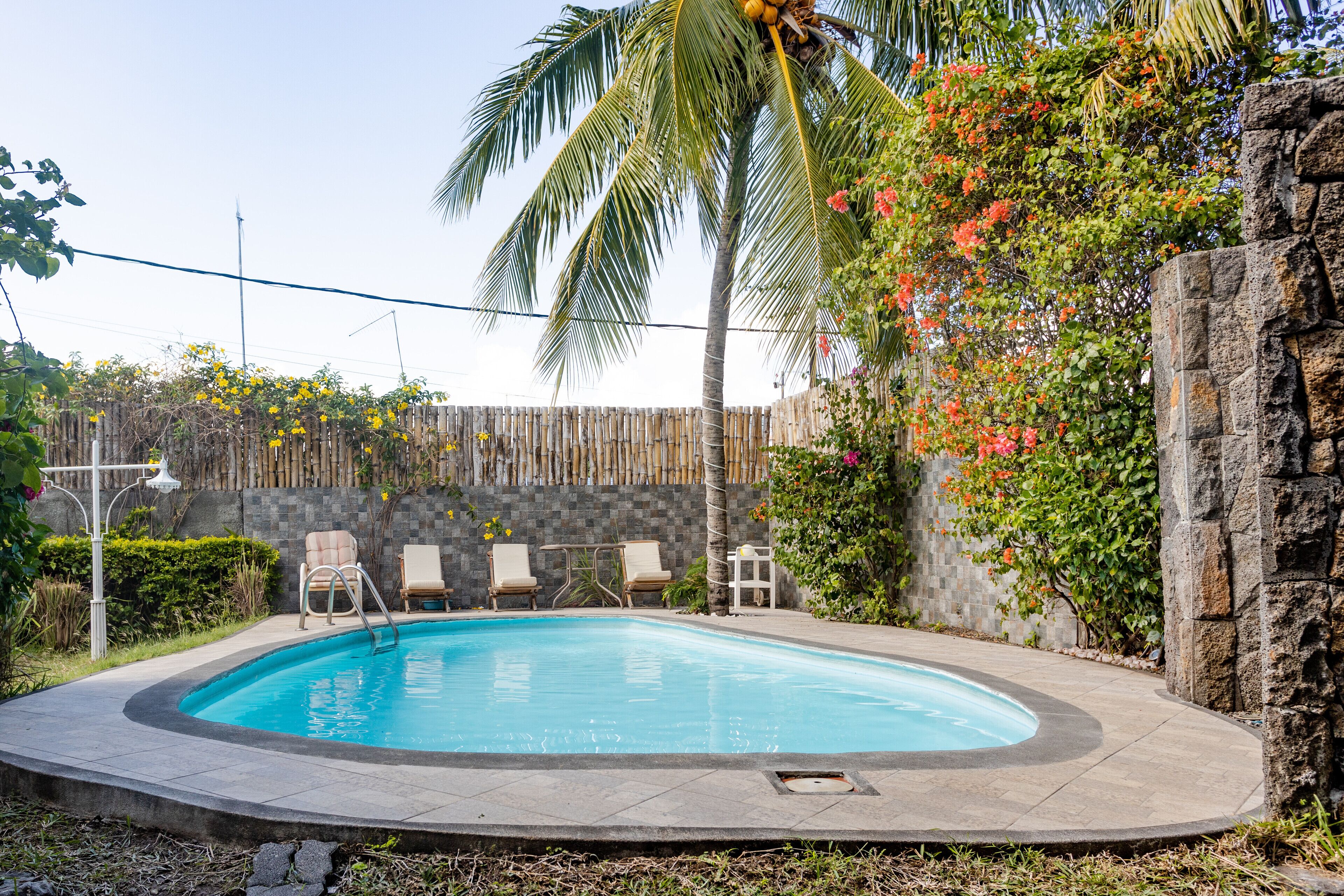 Une piscine bordée de pierres, entourée de chaises longues et d’une clôture en bois.