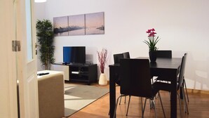 A modern living room with a dining area, including a flat-screen TV, a dining table with chairs, and a cityscape painting on the wall. - Family House in central Lisbon (Lisboa)