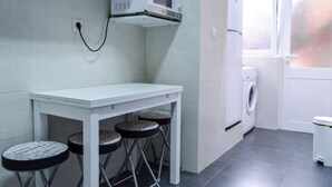 A compact kitchen with a microwave, washing machine, and a small dining table with stools. - Family House in central Lisbon (Lisboa)
