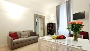 Una sala de estar moderna con un sofá, una mesa de comedor con sillas, una estantería y un televisor montado en la pared.