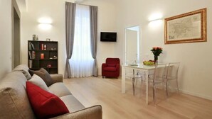 Una sala de estar moderna con un sofá, una mesa de comedor con sillas, un sillón rojo, una estantería y un televisor de pantalla plana montado en la pared.