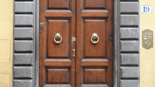 Una puerta doble de madera con un aldabón de metal, enmarcada en un arco de piedra.