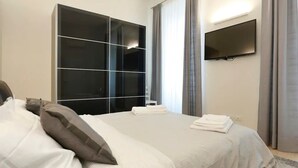 Habitación de hotel con cama, un armario negro grande, televisor de pantalla plana y ventana con cortinas.