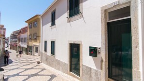 A cobblestone street with buildings on either side, a dog walking, and a person standing. - Casa Sanches (Cascais)