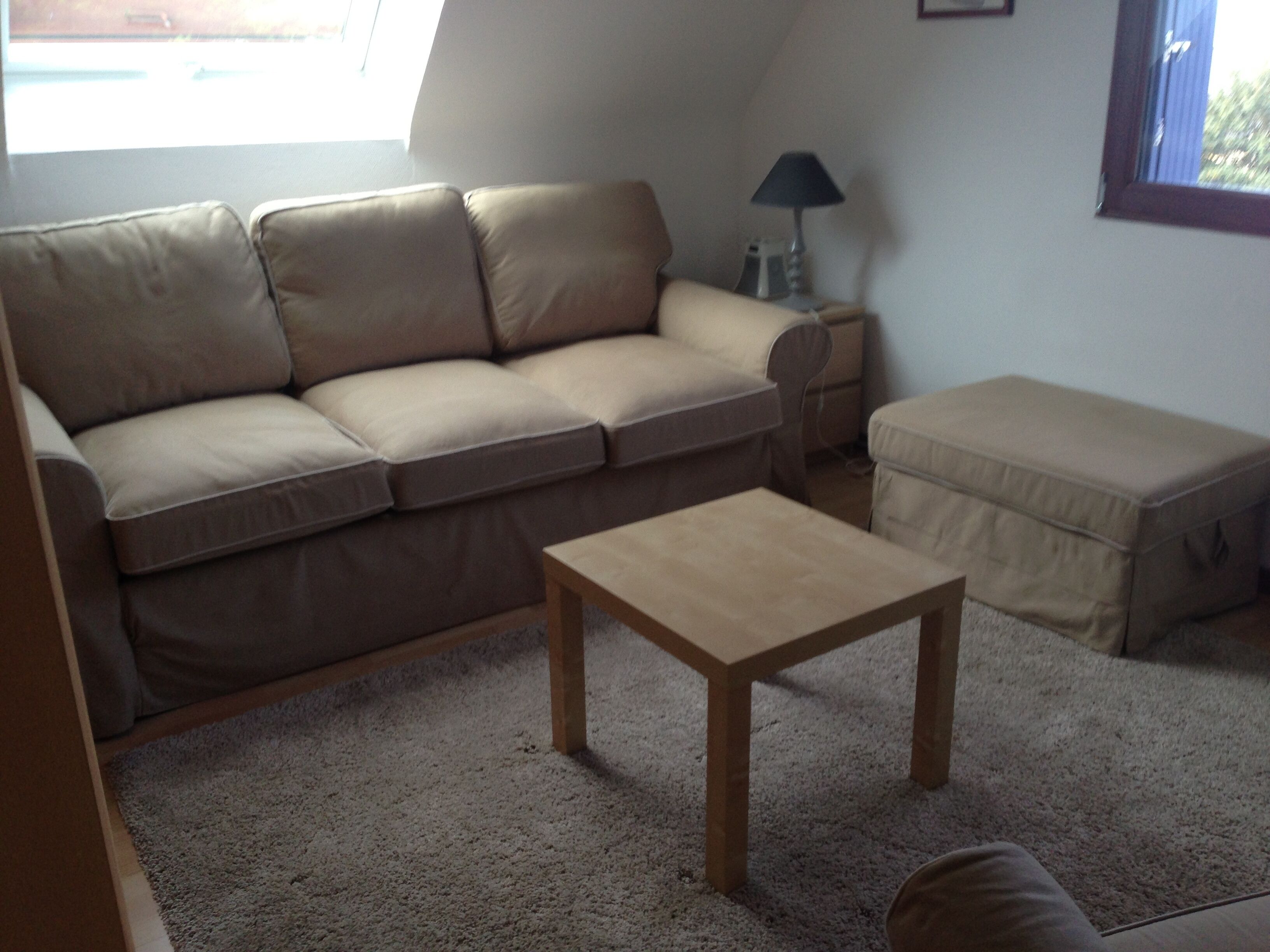 A living room with a beige sofa, a wooden coffee table, and a small ottoman.